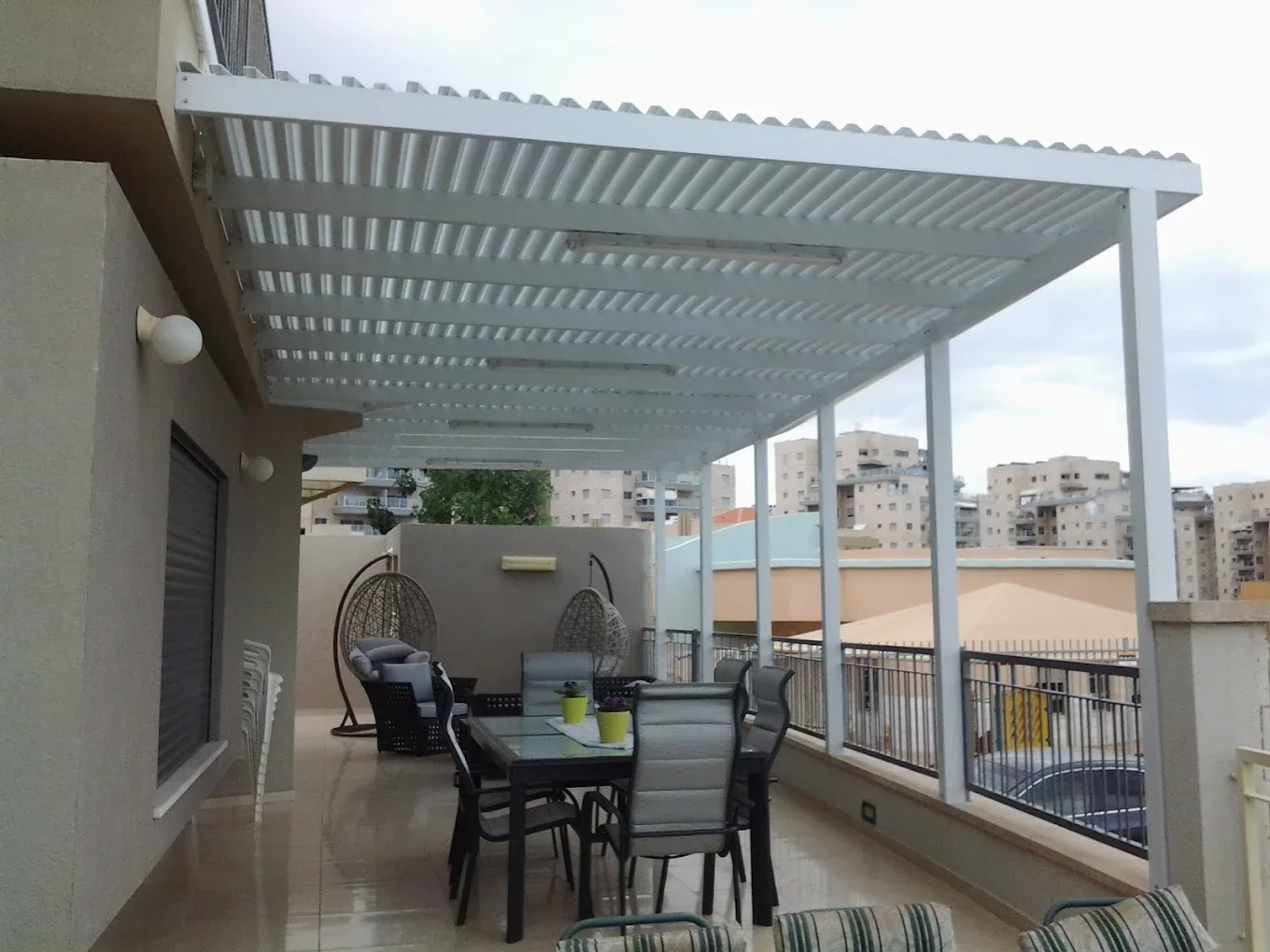 פרגולה לבנה עם רפפות מעל שולחן במרפסת