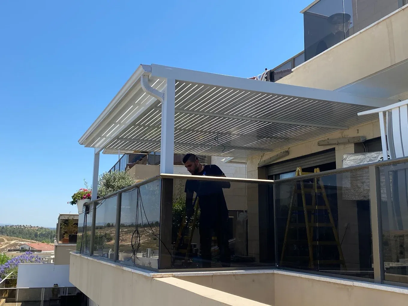 פרגולה לבנה במרפסת עליונה עם מעקה זכוכית