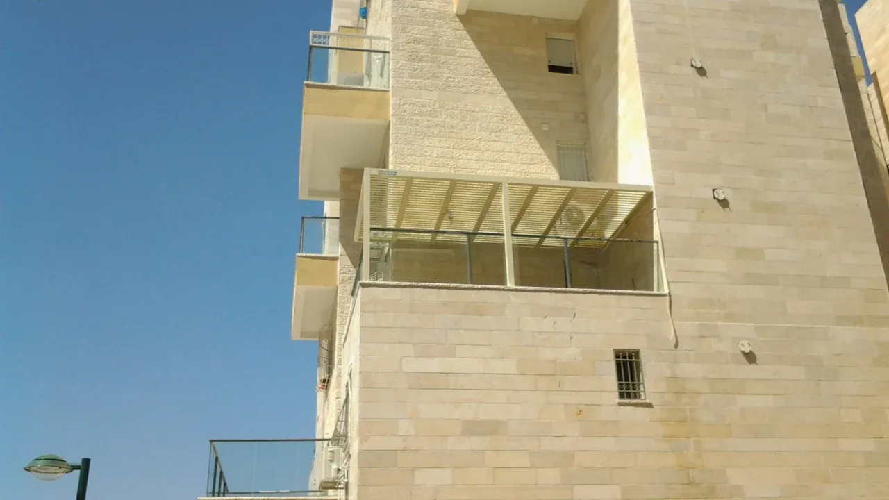 פרגולה לבנה במרפסת בניין מחופה אבן