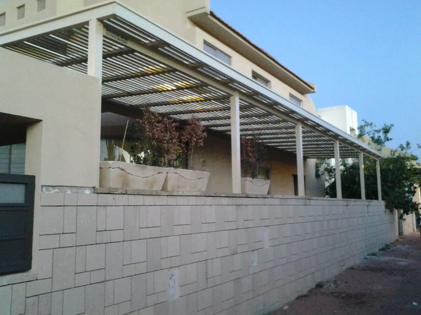 פרגולת רפפות לבנה ארוכה בחזית הבית