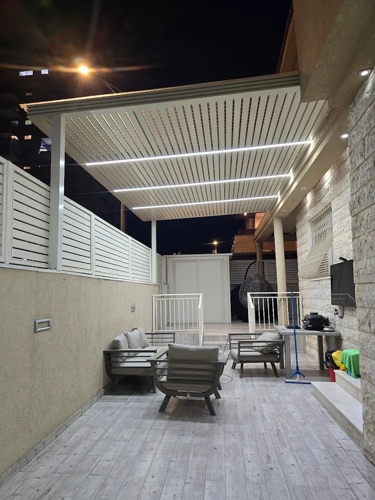 פרגולה לבנה מוארת מעל פינת ישיבה בחצר צרה