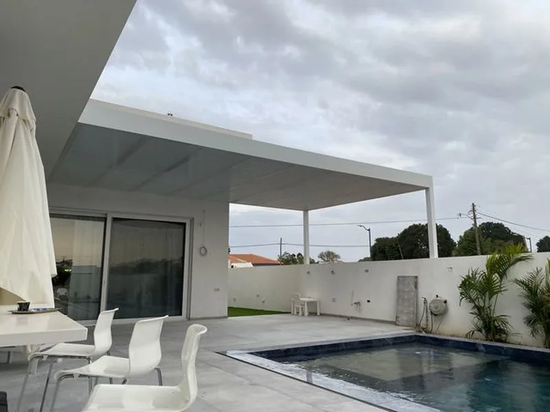 פרגולה לבנה מעל פינת ישיבה לצד בריכת שחייה